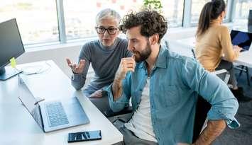 Two colleagues working on a project over a lap top in a casual business model office.