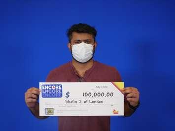 Shafin Jiwani holds up his winning lottery cheque for $100,000. (Photo courtesy of OLG)