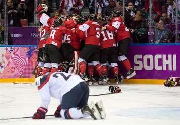 USA's Michelle Picard kneels on the ice as Canada celebrates their overtime win in the gold medal hockey game at the Sochi Winter Olympics Thursday February 20, 2014 in Sochi, Russia. Canada's men will play the United States in semi-final action Friday. THE CANADIAN PRESS/Adrian Wyld