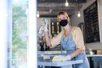 Coffee shop owner working with face mask and gloves , cleaning and disinfecting tables. © Can Stock Photo / halfpoint