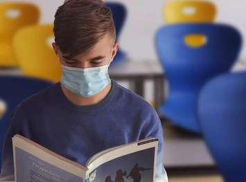 A student reads a book while wearing a mask. (Photo from Pixabay)